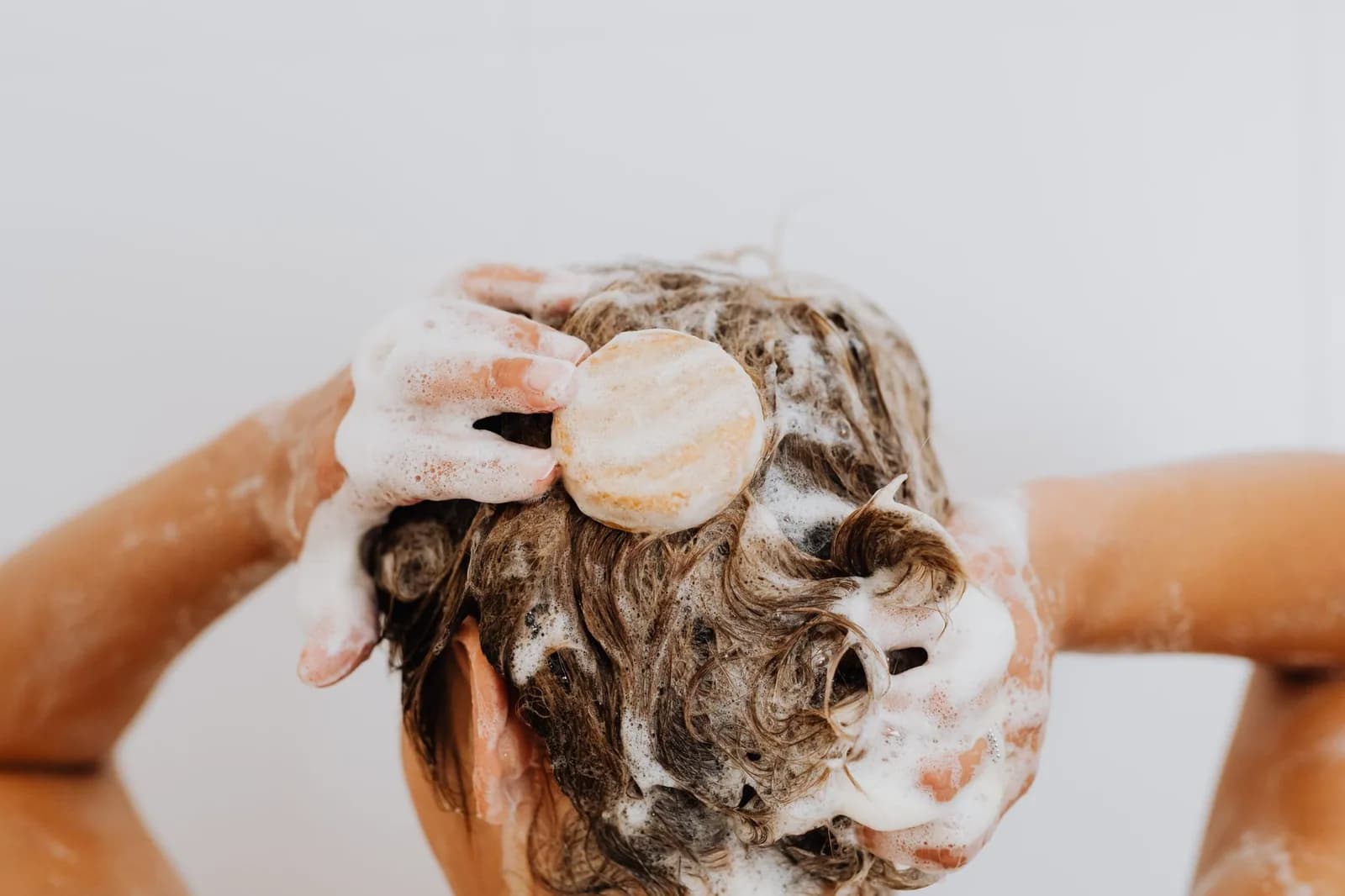 Hands working a bar of soap into a lather in long wet hair