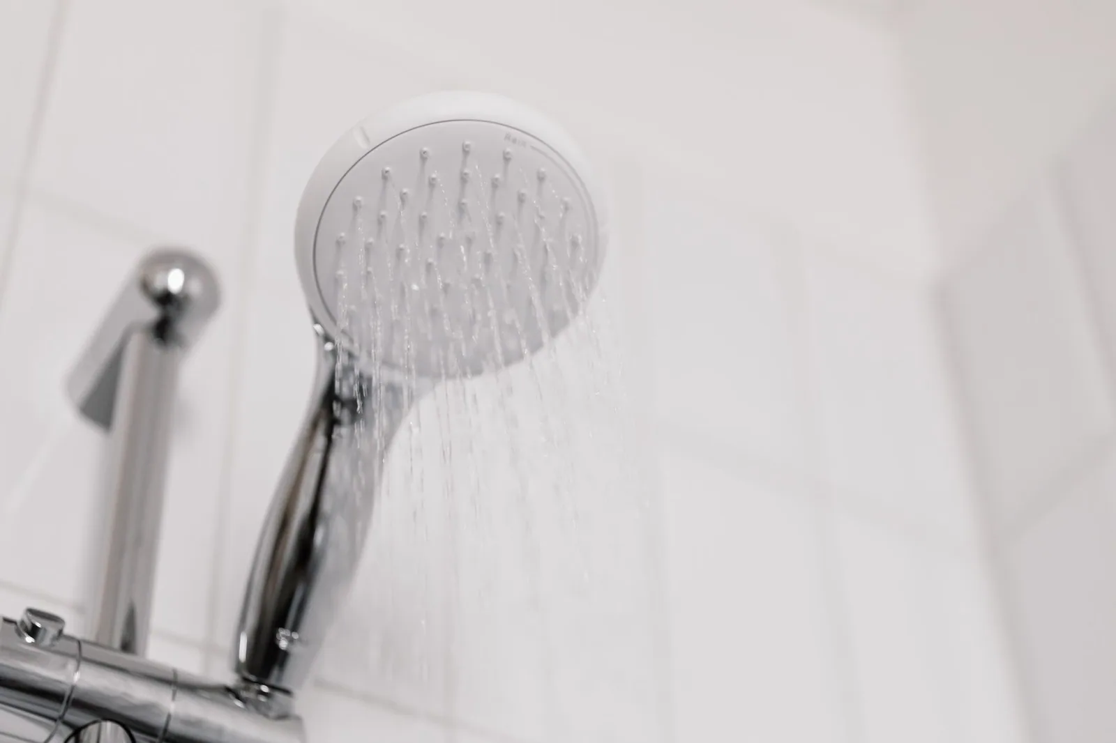 Water streaming from a chrome shower head in a white tiled bathroom