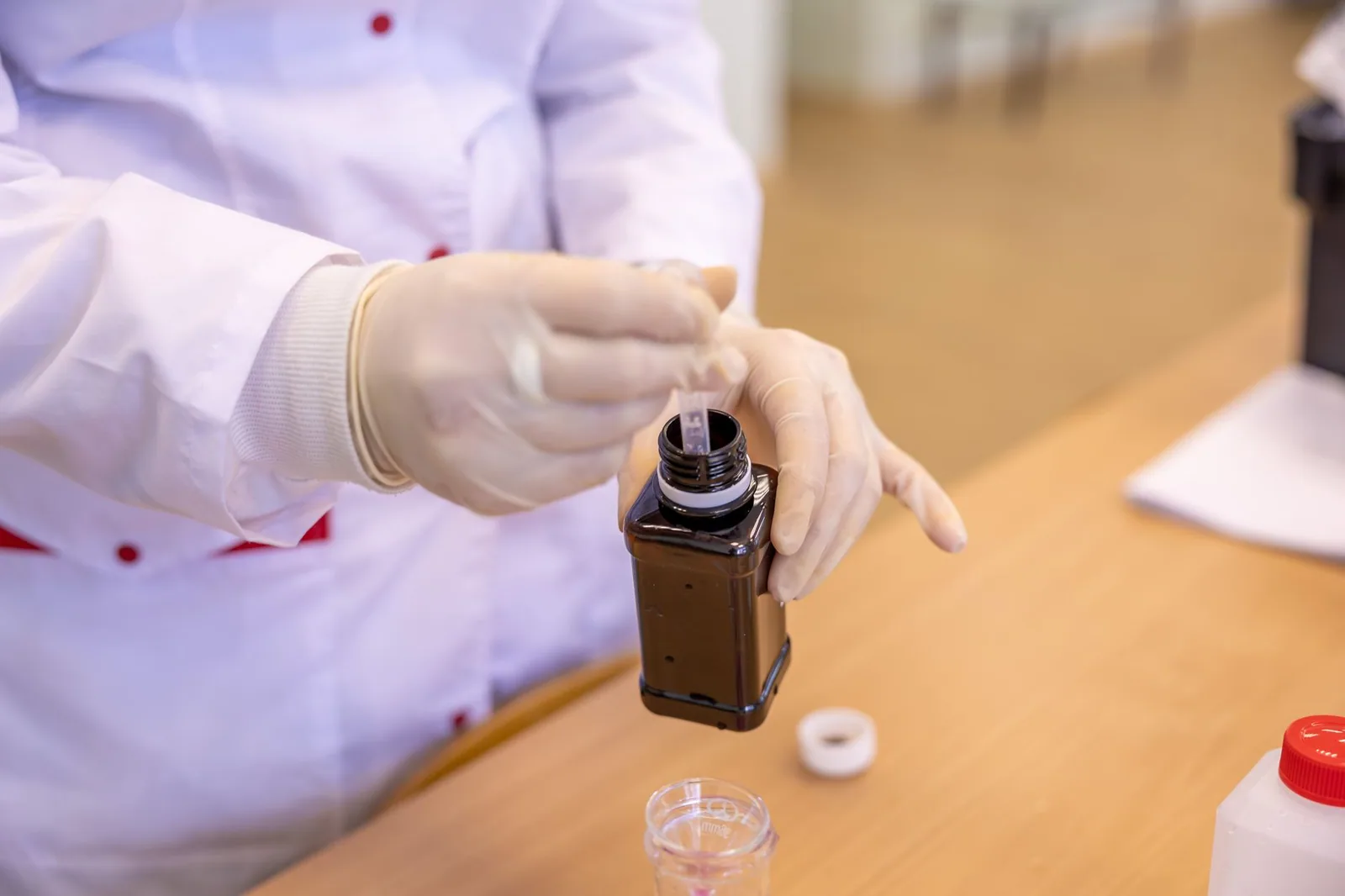 A technician in protective gear drawing a liquid sample from a bottle